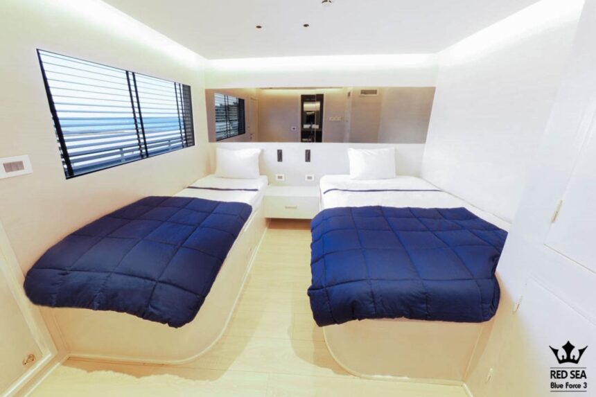 Twin cabin aboard the Blue Force 3 with navy bedspreads and a window with blinds