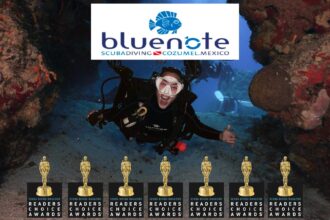 Scuba diver smiling through a reef swim-through beneath the Blue Note Scuba Cozumel logo and awards row