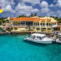 Buddy Dive Resort in Bonaire with two dive boats docked beside turquoise water and yellow buildings