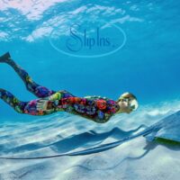 Freediver in a colorful SlipIns diveskin gliding past a stingray over sand