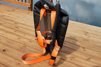 Deep 6 single tank wing with orange harness webbing and corrugated inflator hose, standing on a wooden dock