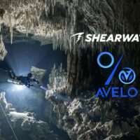 Cave diver with a primary light exploring a stalactite filled cavern, Shearwater and Avelo Labs logos overlaid