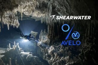 Cave diver with a primary light exploring a stalactite filled cavern, Shearwater and Avelo Labs logos overlaid
