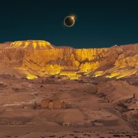 Total solar eclipse diamond ring effect over an illuminated temple below desert cliffs at night
