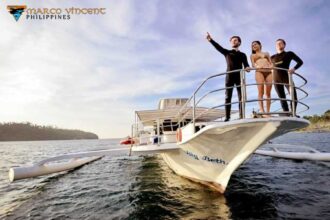 Three divers posing on the stern of a Marco Vincent Philippines outrigger boat at sunset