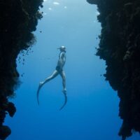 Freediver descending a rope through a narrow underwater canyon in open blue water