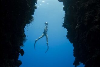 Freediver descending a rope through a narrow underwater canyon in open blue water