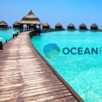 Wooden dock leading to overwater bungalows on a turquoise lagoon, overlaid with the Ocean First logo
