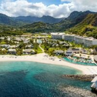 Aerial view of the Sandals Saint Vincent resort beach, pools and overwater villa framed by green mountains