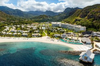 Aerial view of the Sandals Saint Vincent resort beach, pools and overwater villa framed by green mountains