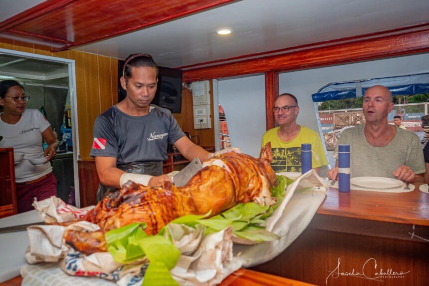 crew member carving a roasted pig for guests at the dining table