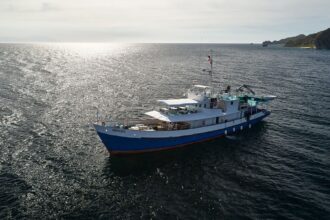 Aerial view of the liveaboard M/Y Resolute anchored on calm water under low sun