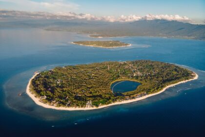 Aerial view of a Gili island ringed by white sand and shallow reef, with Lombok rising in the distance