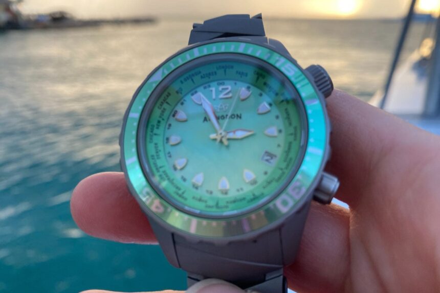 Close-up of the Abingdon Marina dial and world city bezel held in front of a harbor at dusk