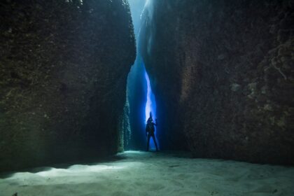 Diver silhouetted in the narrow sunlit canyon of Leru Cut in the Solomon Islands above a sand floor