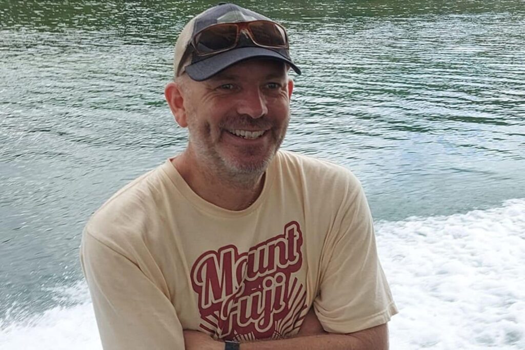 Portrait of Sam Leeson smiling on a boat wearing a Mount Fuji t-shirt
