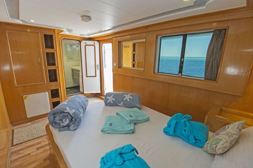 Wood-paneled cabin aboard the Golden Dolphin II with bed, rolled towels and ocean-view window