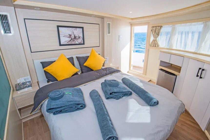 Cabin bed with yellow pillows and rolled towels aboard the SS Glorious Miss Nouran, overlooking the sea