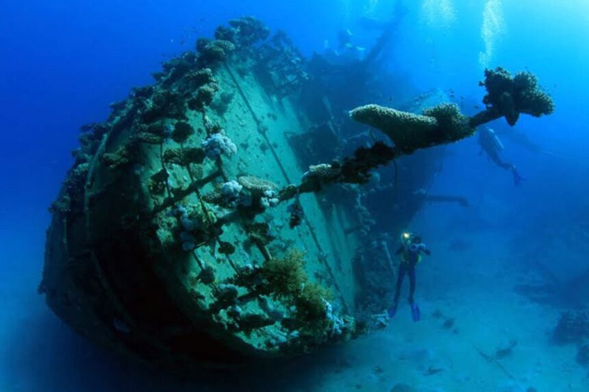 diver exploring a large shipwreck encrusted with coral