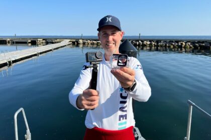 DIVEIN tester holding the DJI Osmo Action 5 Pro on a grip alongside its dive housing at a harbour