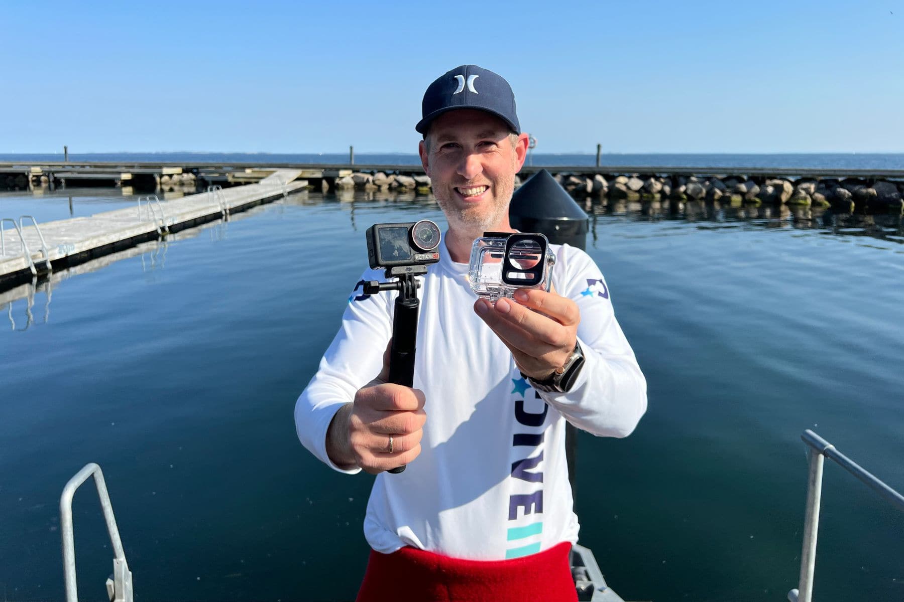 DIVEIN tester holding the DJI Osmo Action 5 Pro on a grip alongside its dive housing at a harbour