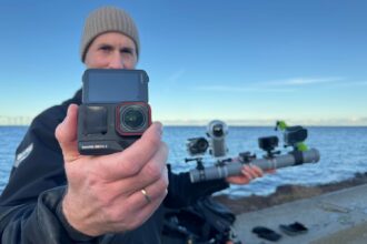 Our tester holding the Insta360 Ace Pro 2 up to the lens with a multi camera test rig by the water behind