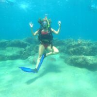 Diver striking a yoga tree pose underwater, giving the OK signal with both hands over a reef
