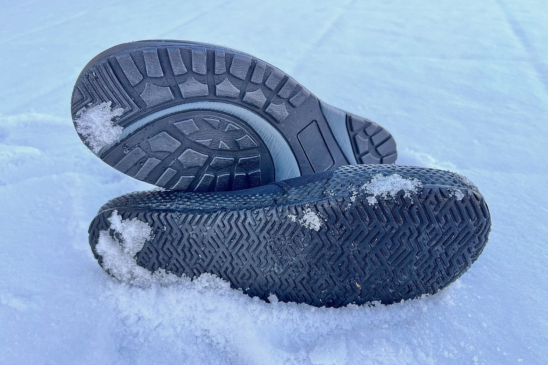Two dive boots lying sole up in fresh snow so the tread patterns can be compared