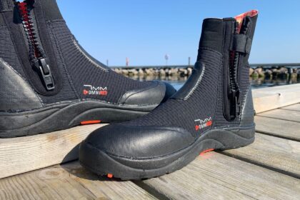 Side view of the BARE 7mm Ultrawarmth boots with red zips, standing on a dock by the harbour