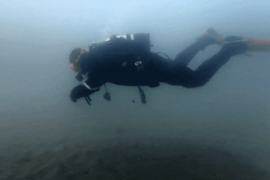 Diver in a black drysuit swimming horizontally through cold, silty water during DIVEIN drysuit testing