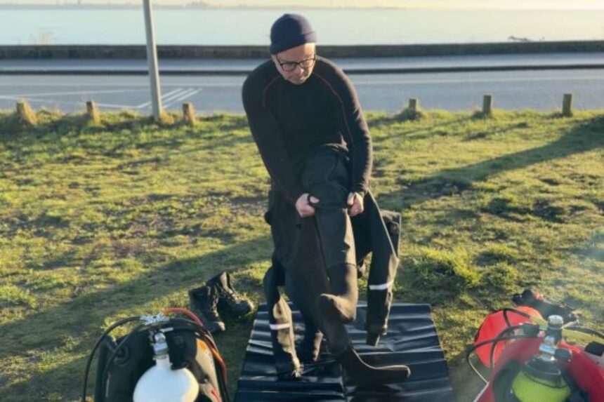Donning The Hollis DX-300X Drysuit Our tester stepping into the Hollis DX-300X drysuit legs on a changing mat beside twin cylinders