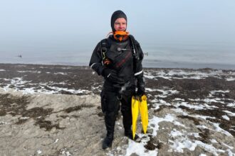DIVEIN tester fully kitted in the Hollis DX-300X drysuit on a snowy shore, yellow fins in hand