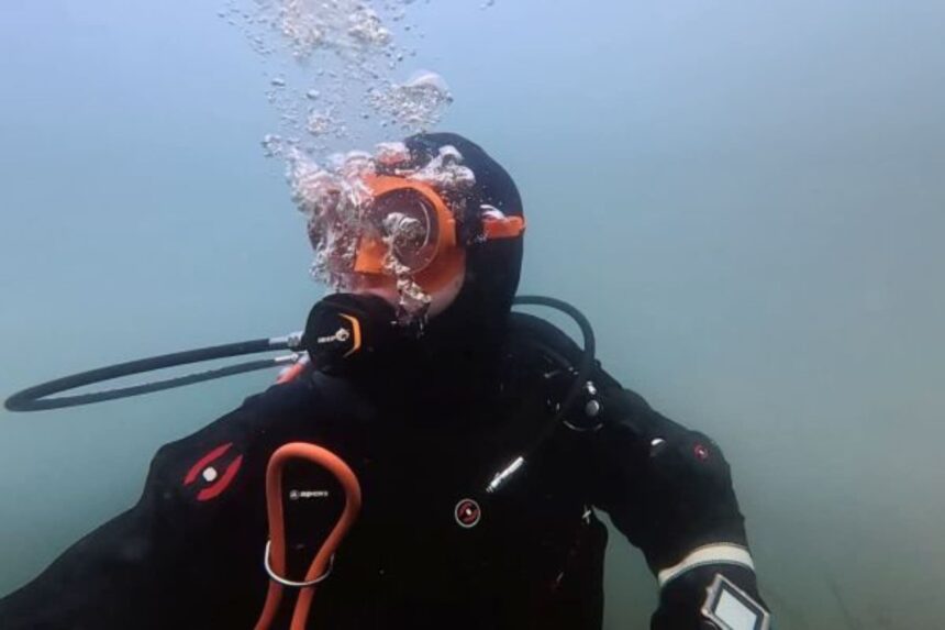 Mask Testing Underwater With Bubbles Our tester exhaling a stream of bubbles underwater while wearing an orange-framed mask and drysuit