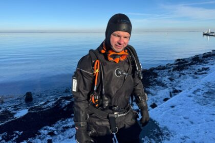 DIVEIN tester standing in the water in the Northern Diver HID drysuit beside a snow-covered shoreline