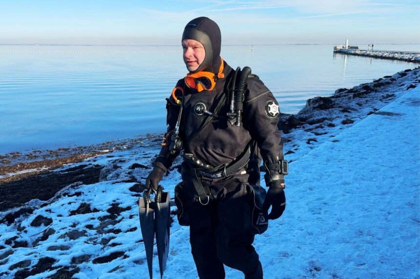 Northern Diver HID Drysuit On Snowy Shore DIVEIN tester walking a snowy shoreline in the Northern Diver HID drysuit with fins in hand