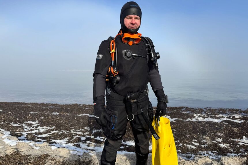 BARE Sentry Tech Full Kit DIVEIN tester geared up in the BARE Sentry Tech drysuit on a snowy shore, yellow fins in hand