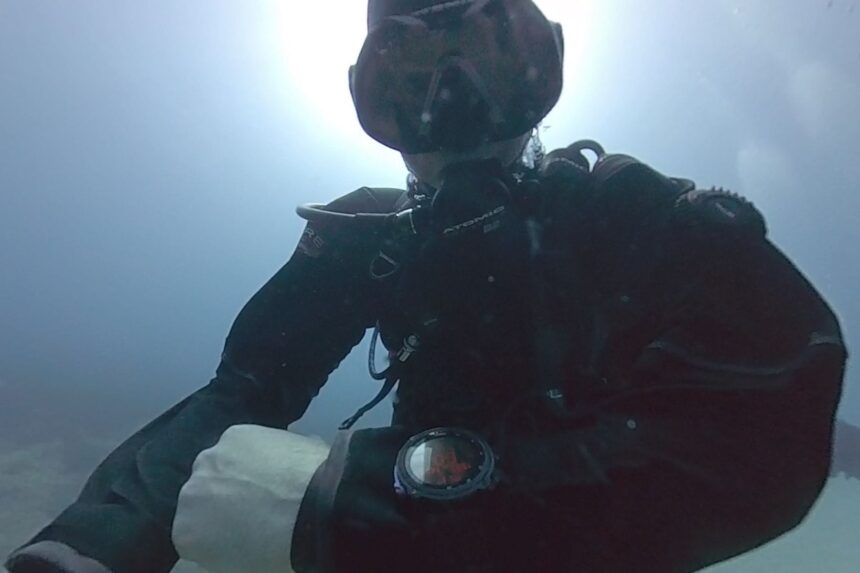 BARE X-Mission Evolution Long Dive DIVEIN tester checking a wrist dive computer underwater in the BARE X-Mission Evolution drysuit