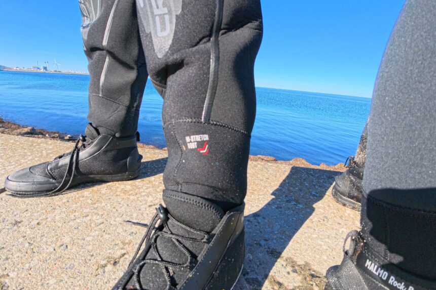 Laced rock boots and ankle section of the Cressi Desert drysuit on a sunny shoreline