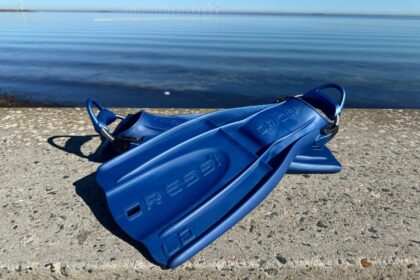 Blue Cressi Origin fins resting on a concrete quay in front of flat open water