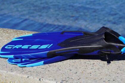 Blue Cressi Maui fins lying on their side on a concrete edge above clear water