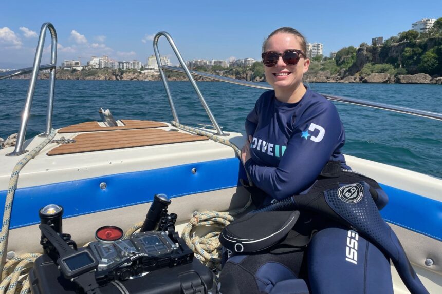 Sylvia Jenkins smiling on a dive boat wearing sunglasses and a DIVEIN rash guard