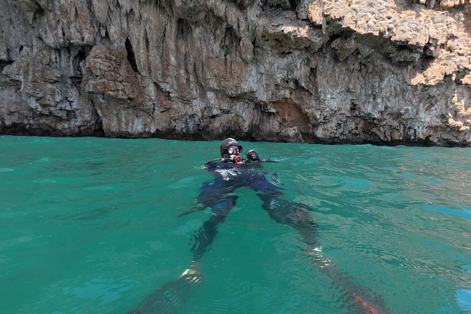 Scuba diver floating at the surface in turquoise water below a rocky cliff face in Turkey