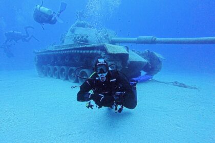 Diver hovering in front of a sunken tank at a Turkish dive site as two more divers pass overhead