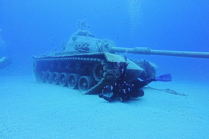 Scuba diver swimming past a sunken military tank resting on the sandy seabed in Turkey
