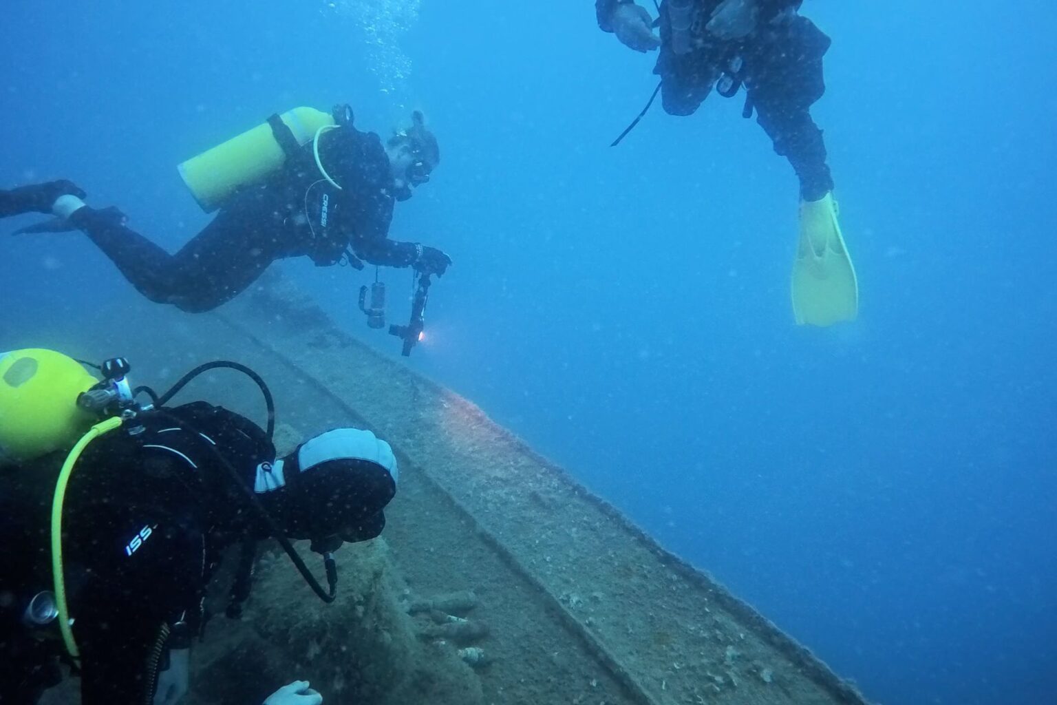 Three scuba divers with a video light working along the hull of a large wreck in Turkey