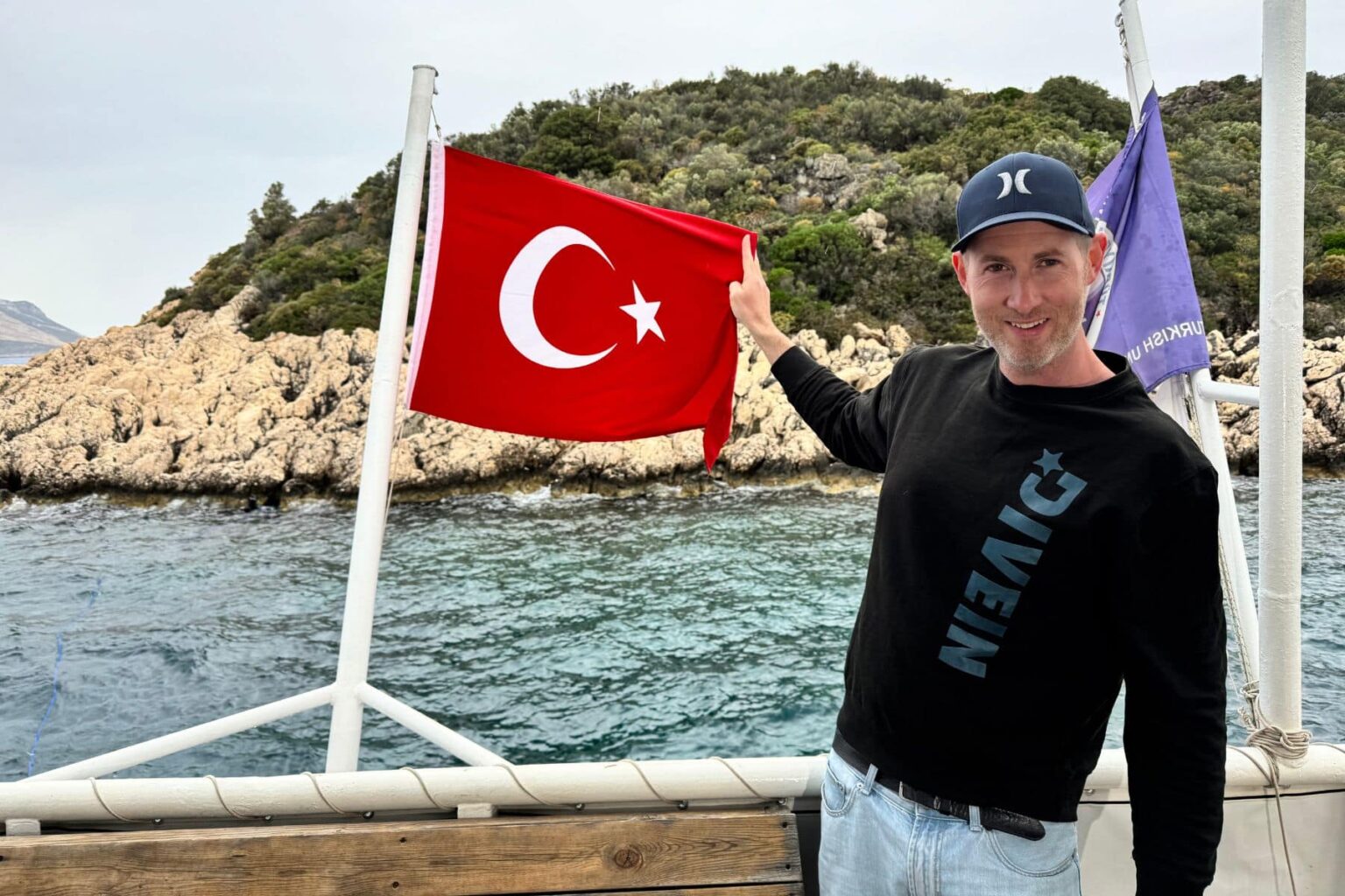 DIVEIN team member in a branded sweater holding the Turkish flag on a dive boat deck