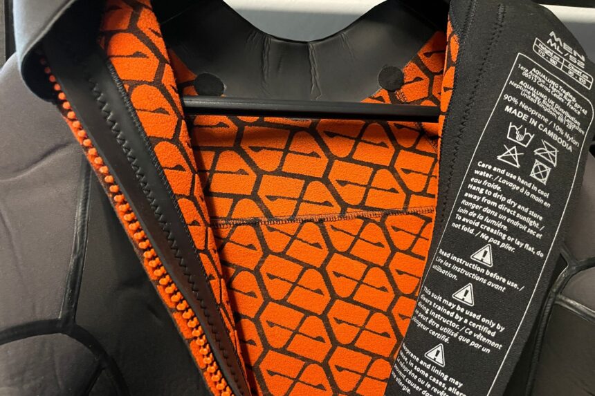 Close-up of the orange patterned lining and back zipper inside the Apeks ThermiQ wetsuit on a hanger