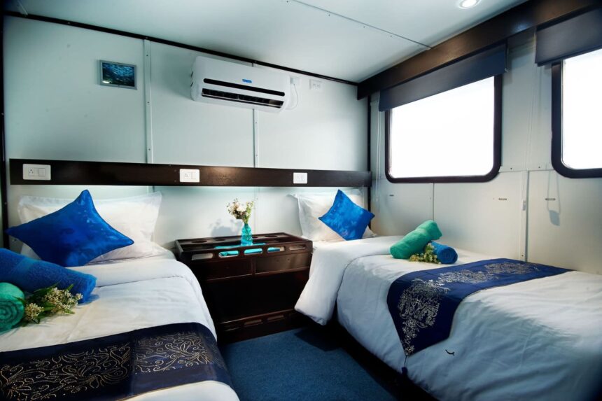 Twin-bed cabin with blue accent pillows, air conditioning unit and a small dresser
