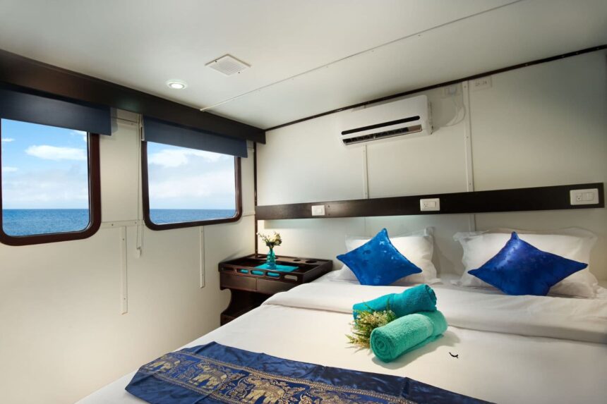 Cabin with a made-up bed, rolled towels and two ocean-view windows