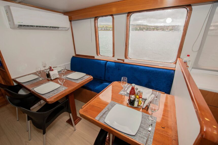 Dining tables set with wine glasses beside large windows overlooking the water